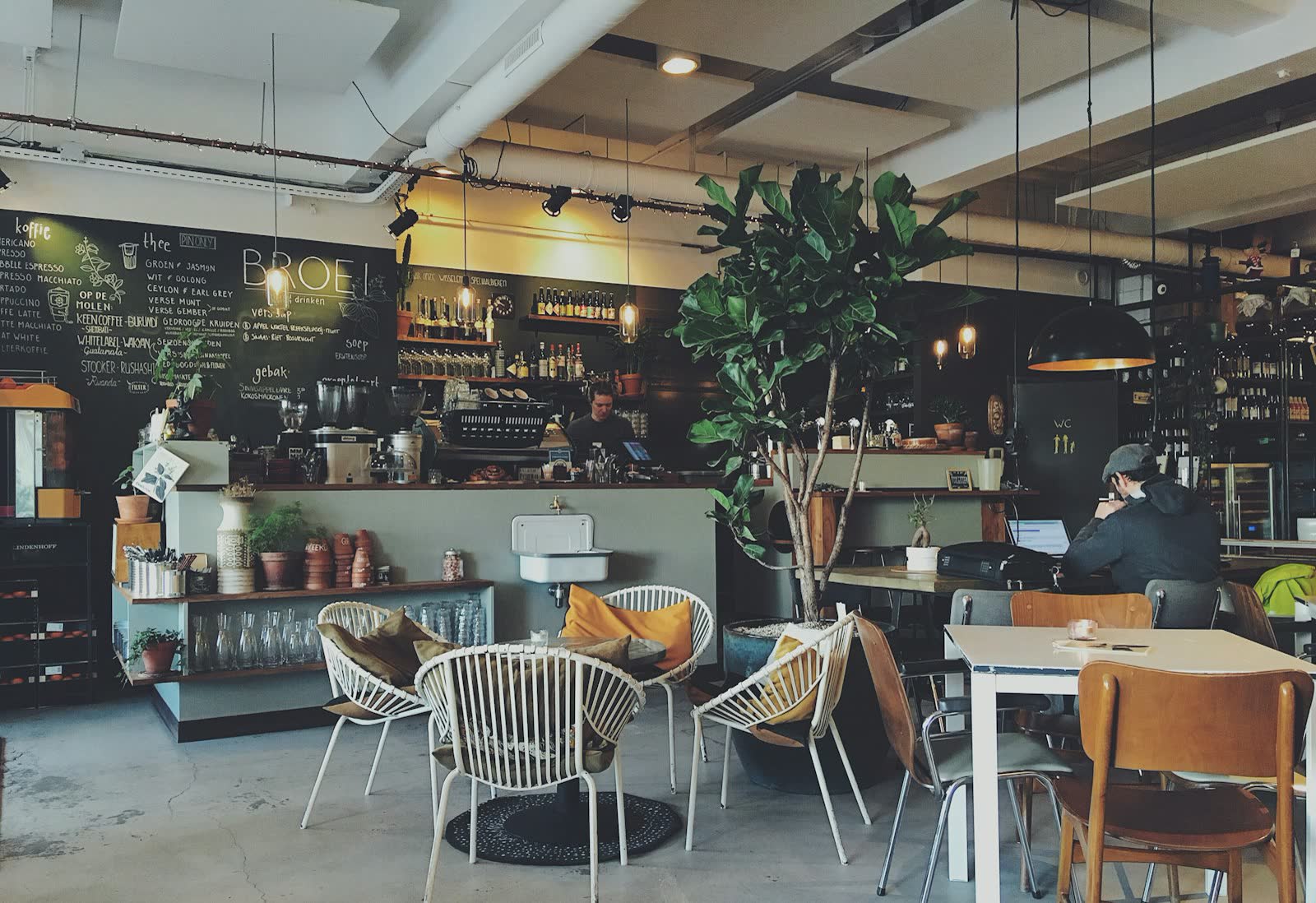 Bright café interior with plants, wooden tables and a long coffee bar